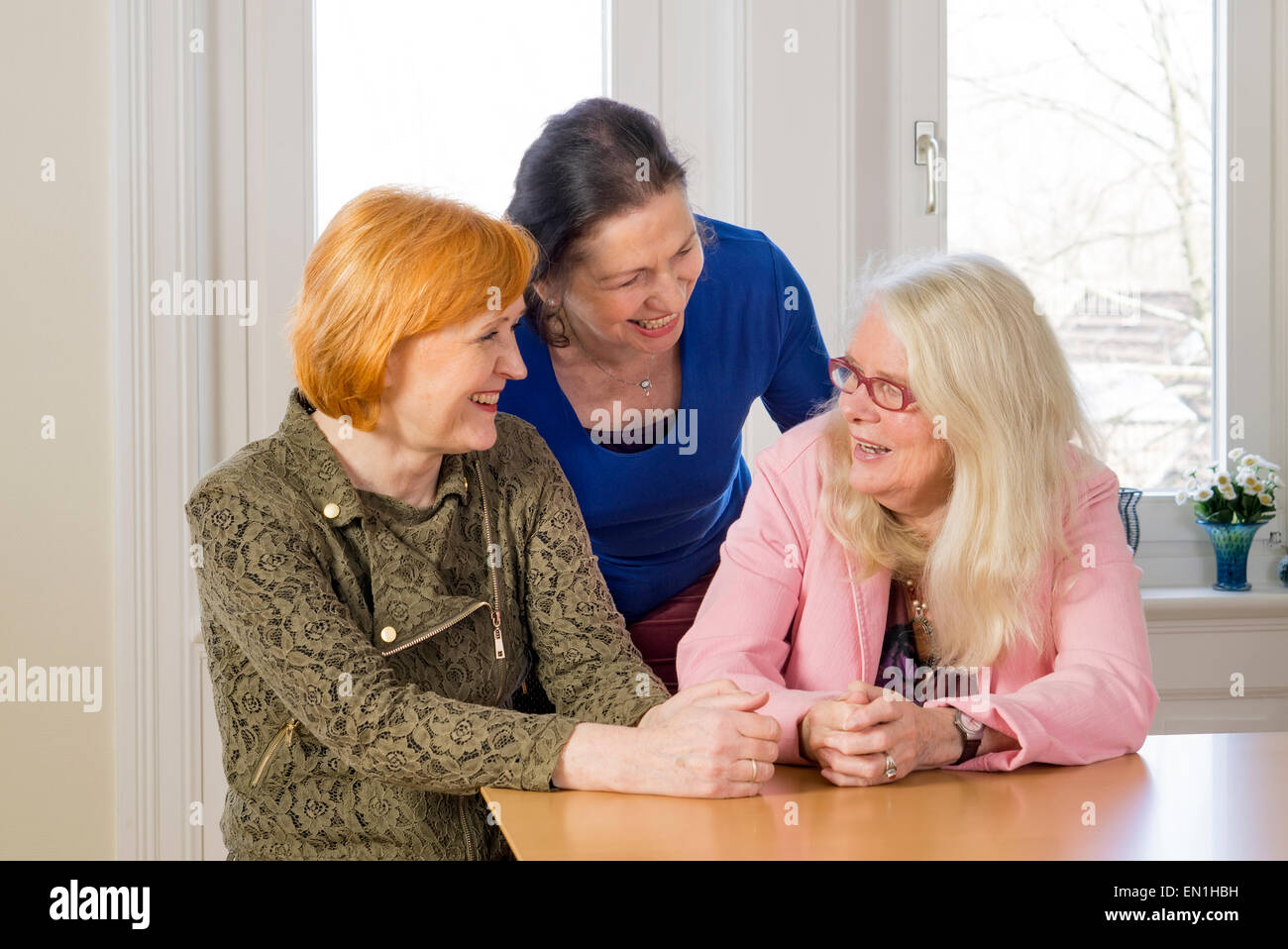 Close up Three Happy Middle Age Women Friends Enjoying their Girl Talk at the Wooden Dining Table Inside a Restaurant. Stock Photo