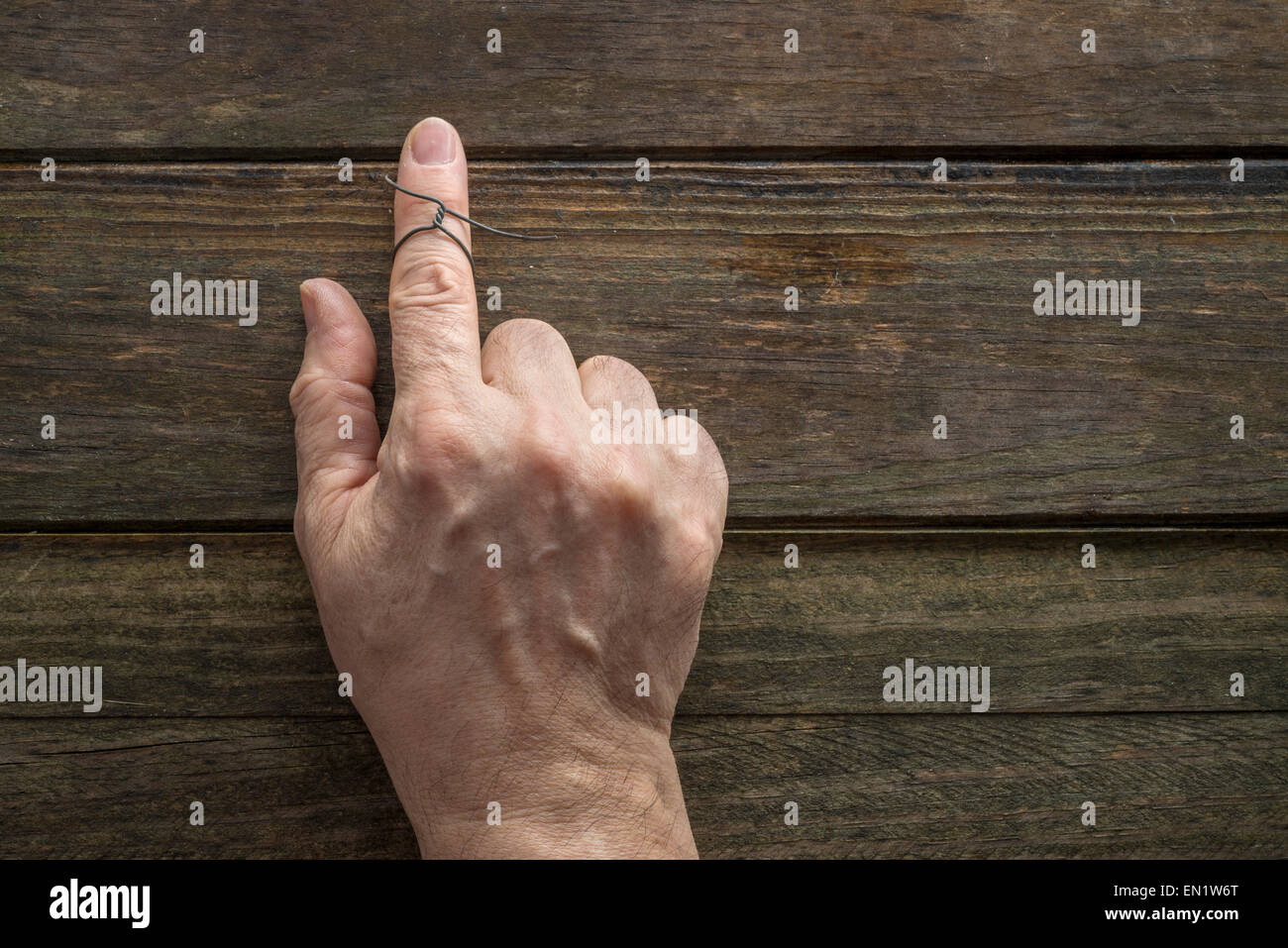 Wire on index finger of an elderly man. Wooden background Stock Photo