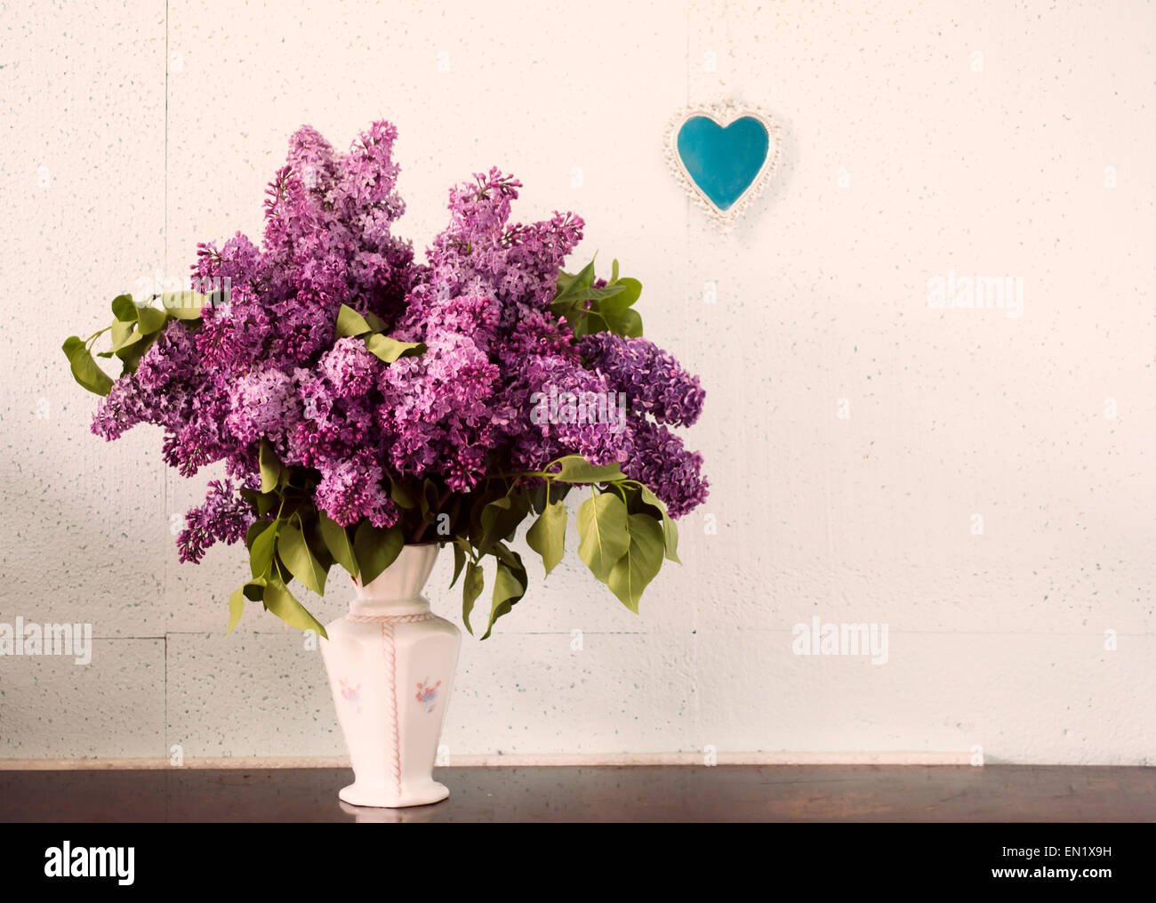 Lilac in a Vase and small heart-shaped mirror on the wall. Stock Photo