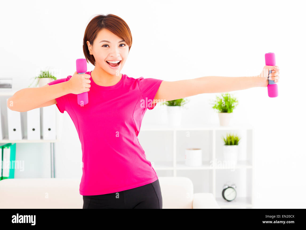 happy young woman exercising with dumbbells in living room Stock Photo