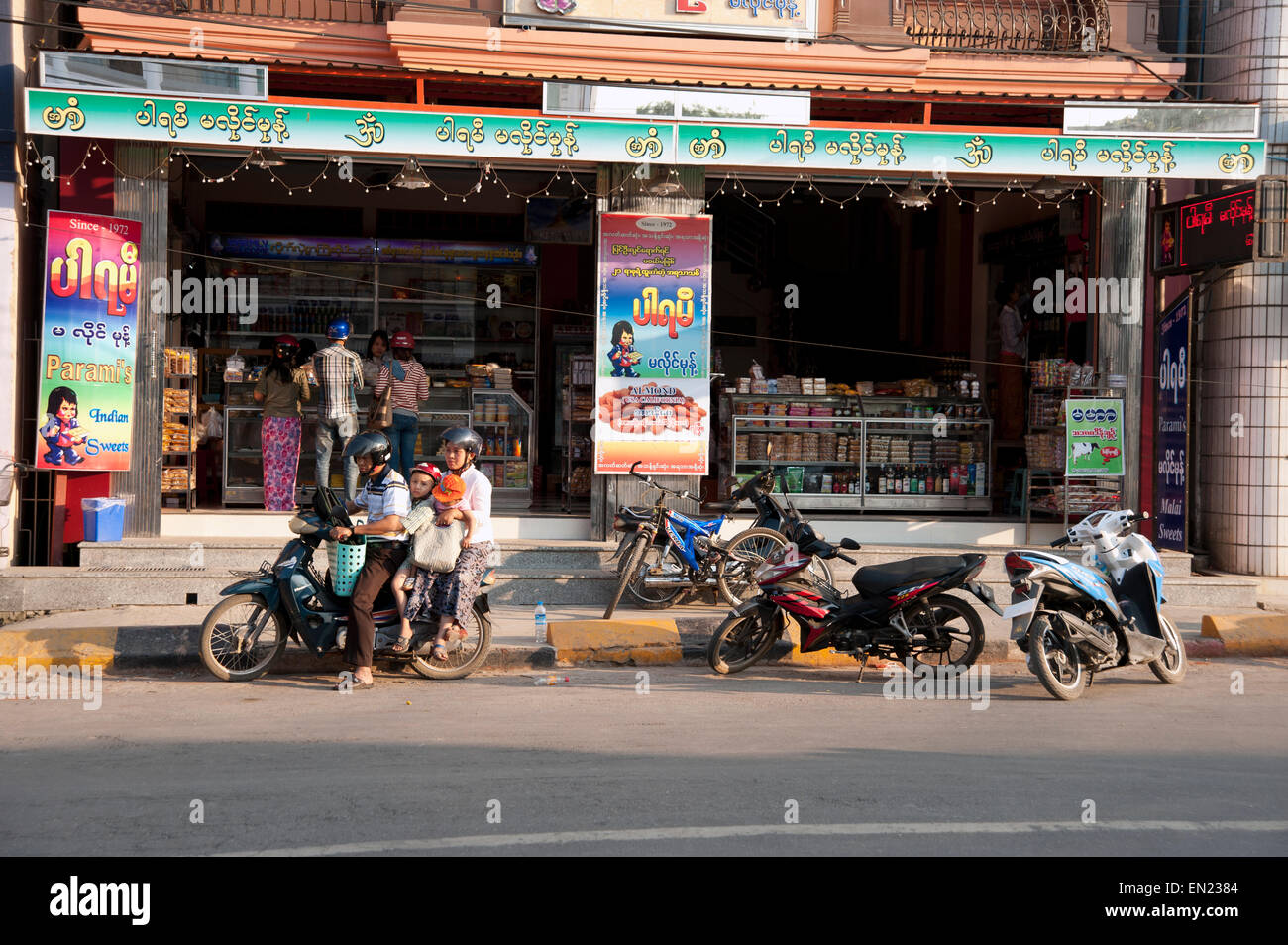 A Burmese family of three prepare to leave a shop on their scooter Stock Photo