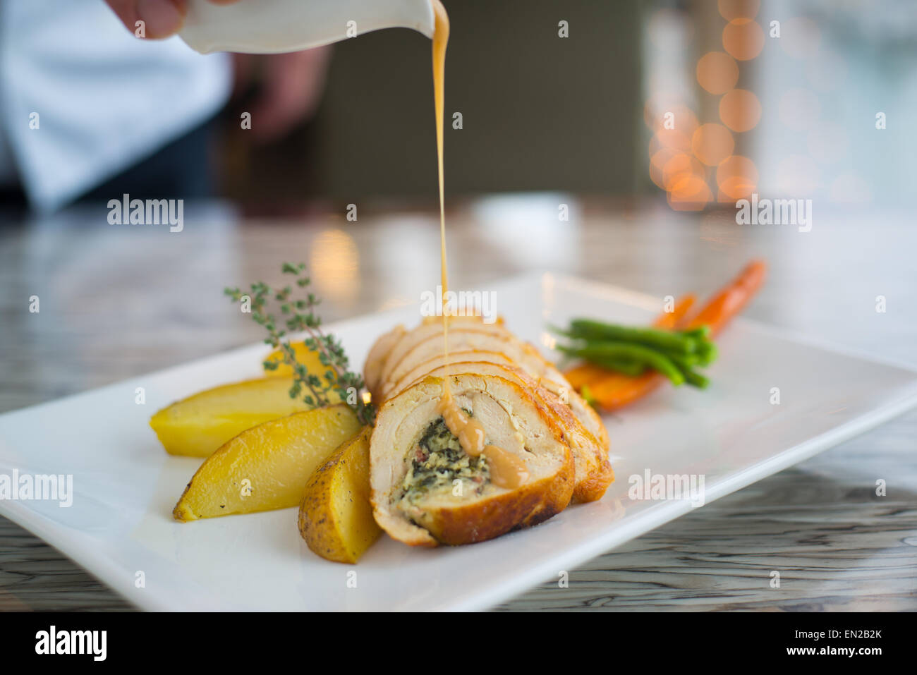 Chicken roulade with sauce drizzled over on white plate with herbs, potato wedges, and vegetables Stock Photo