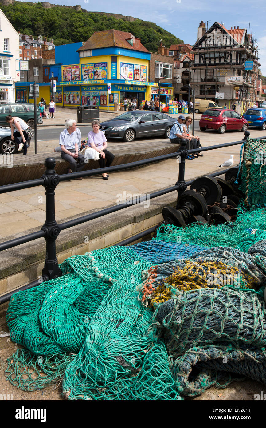 UK, England, Yorkshire, Scarborough, Sandside, visitors sat on bench by fishing nets on working quay Stock Photo