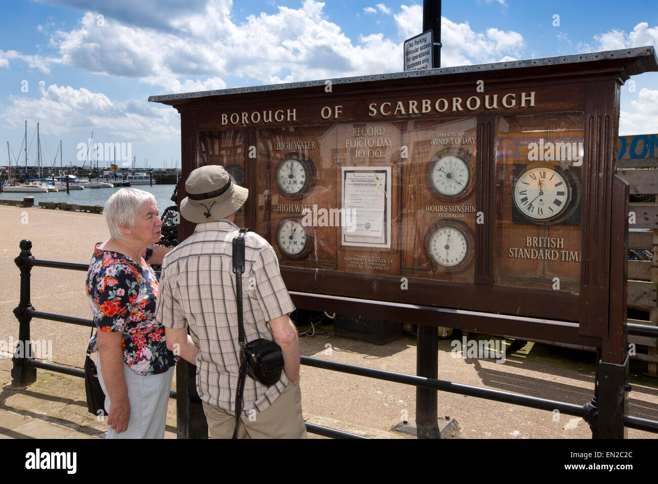 UK, England, Yorkshire, Scarborough, Sandside, mature couple looking at seafront weather and tide board Stock Photo