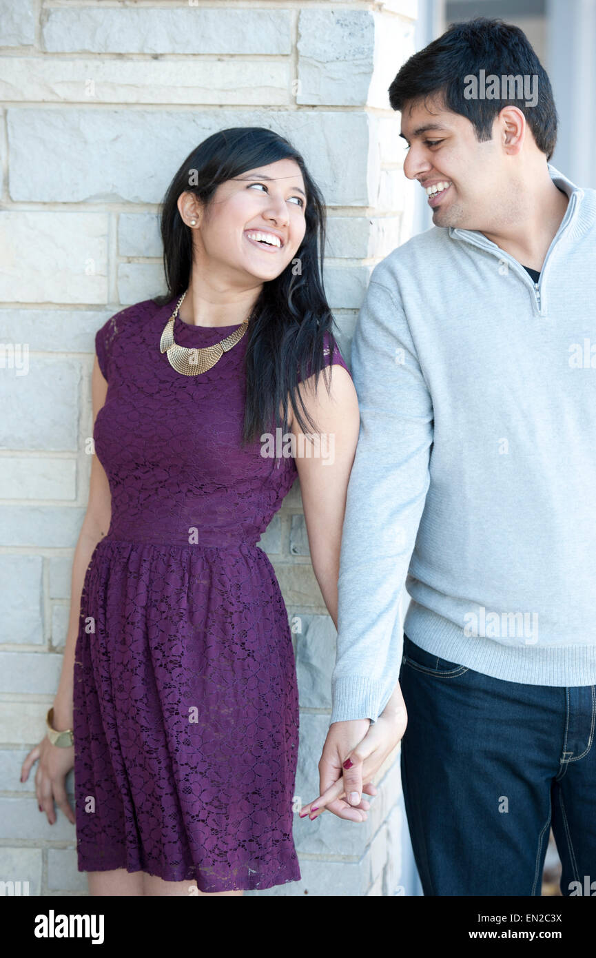 A young and happy Indian couple looking at each other with a brick ...