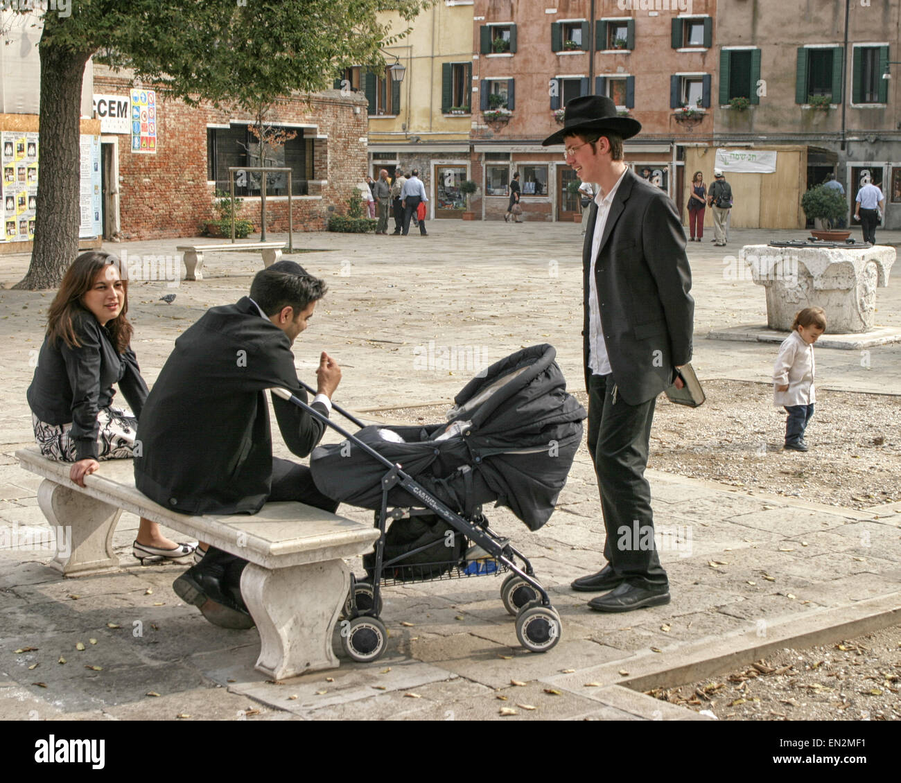 Venice, Province of Venice, ITALY. 7th Oct, 2004. In the Campo del Nuovo Ghetto, the main square of the present-day Venetian Ghetto, a group of Orthodox Jewish inhabitants gather around a bench--a young couple with a baby stroller, a young man, and a small child. Venice, a UNESCO World Heritage Site, is one of the most popular international tourist destinations. © Arnold Drapkin/ZUMA Wire/Alamy Live News Stock Photo