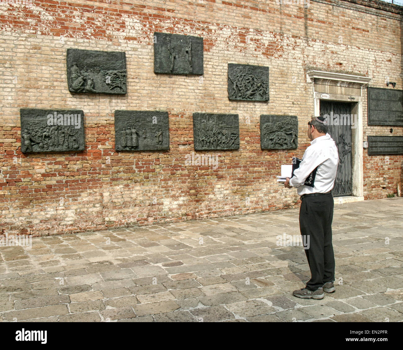 Venice, Province of Venice, ITALY. 7th Oct, 2004. An orthodox Jewish man, holding a prayer book with his prayer shawl under his arm views the seven-panel bronze bas-relief Holocaust memorial, on a wall of the Campo del Nuovo Ghetto by Arbit Blatas, a Lithuanian-born artist who lost his mother in the Holocaust. It commemorates the night of Dec. 5, 1943, when the first 200 of the city's Jews were rounded up and marched out for deportation and death. Venice, a UNESCO World Heritage Site, is one of the most popular international tourist destinations. © Arnold Drapkin/ZUMA Wire/Alamy Live News Stock Photo