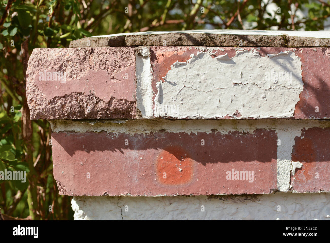 paint peeling off due to weathering - red brick garden wall gatepost cap requiring maintenance and repainting Stock Photo