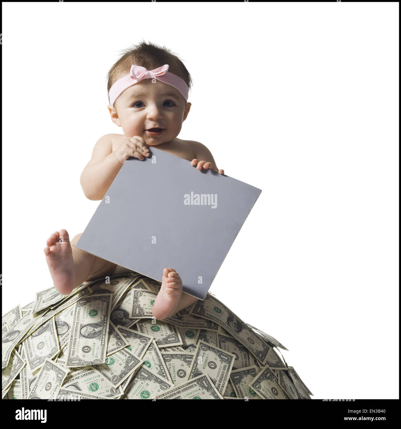 Baby girl sitting on pile of US currency with blank sign Stock Photo
