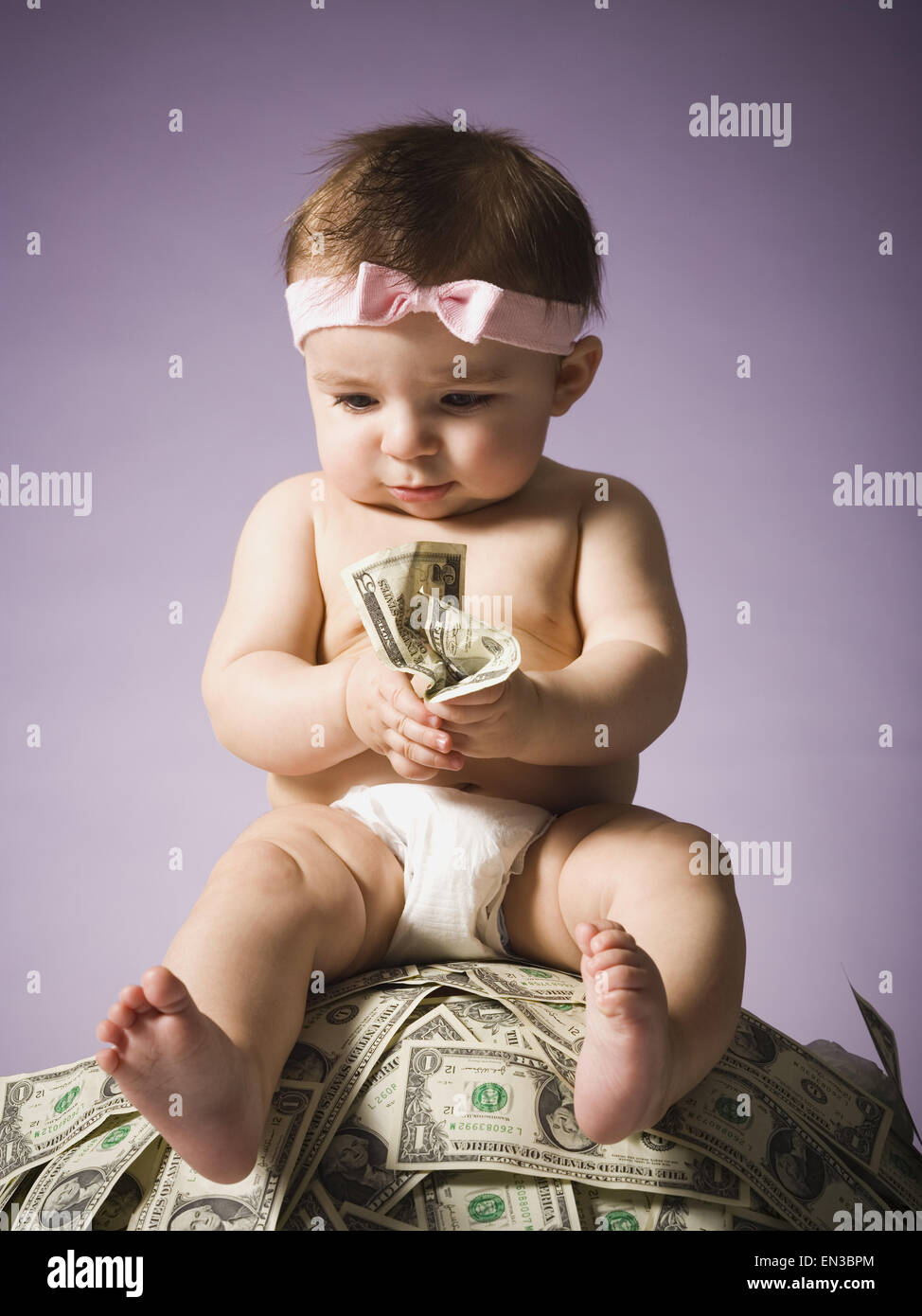 Baby girl sitting on pile of US currency Stock Photo
