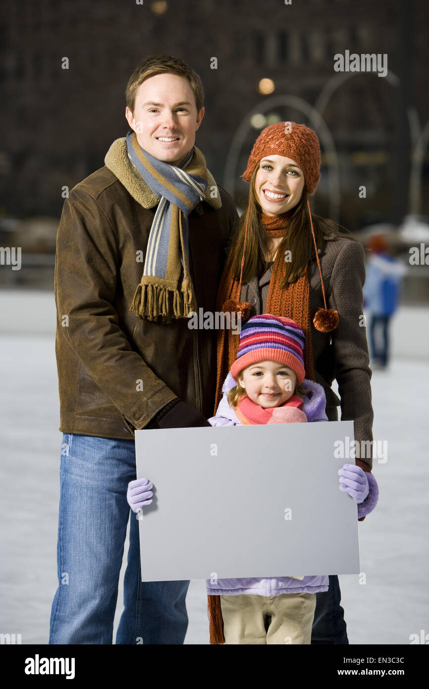 Man and woman with girl holding blank sign outdoors in winter Stock Photo