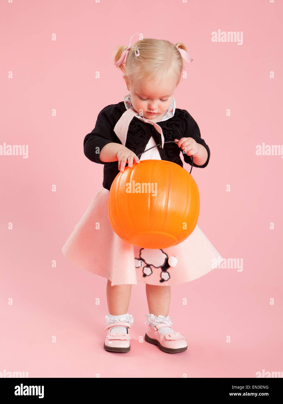 Baby girl (12-17 months) in 1950s style costume, holding pumpkin lantern for Halloween Stock Photo