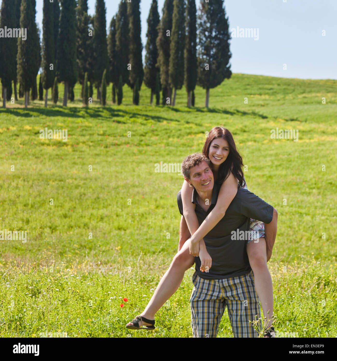 Italy, Tuscany, Man giving piggy back ride to woman on meadow Stock Photo