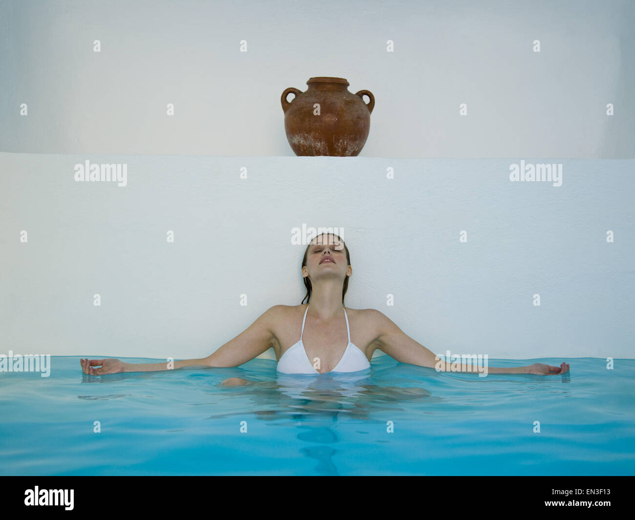 Woman sitting and leaning against wall in pool under urn Stock Photo