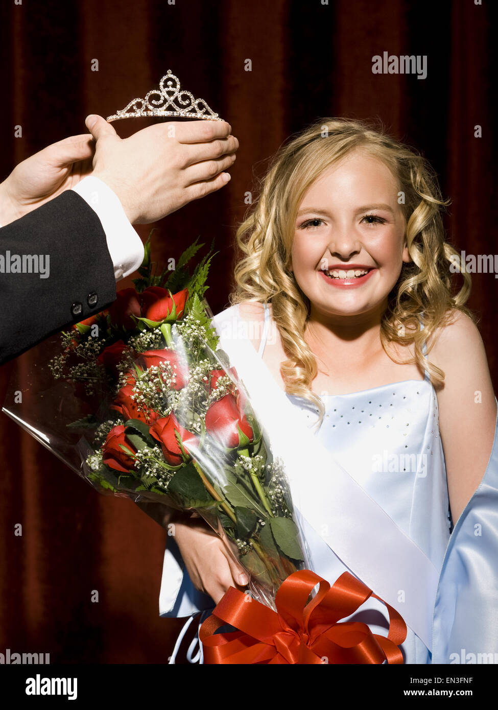 Girl holding red roses being crowned with tiara smiling Stock Photo