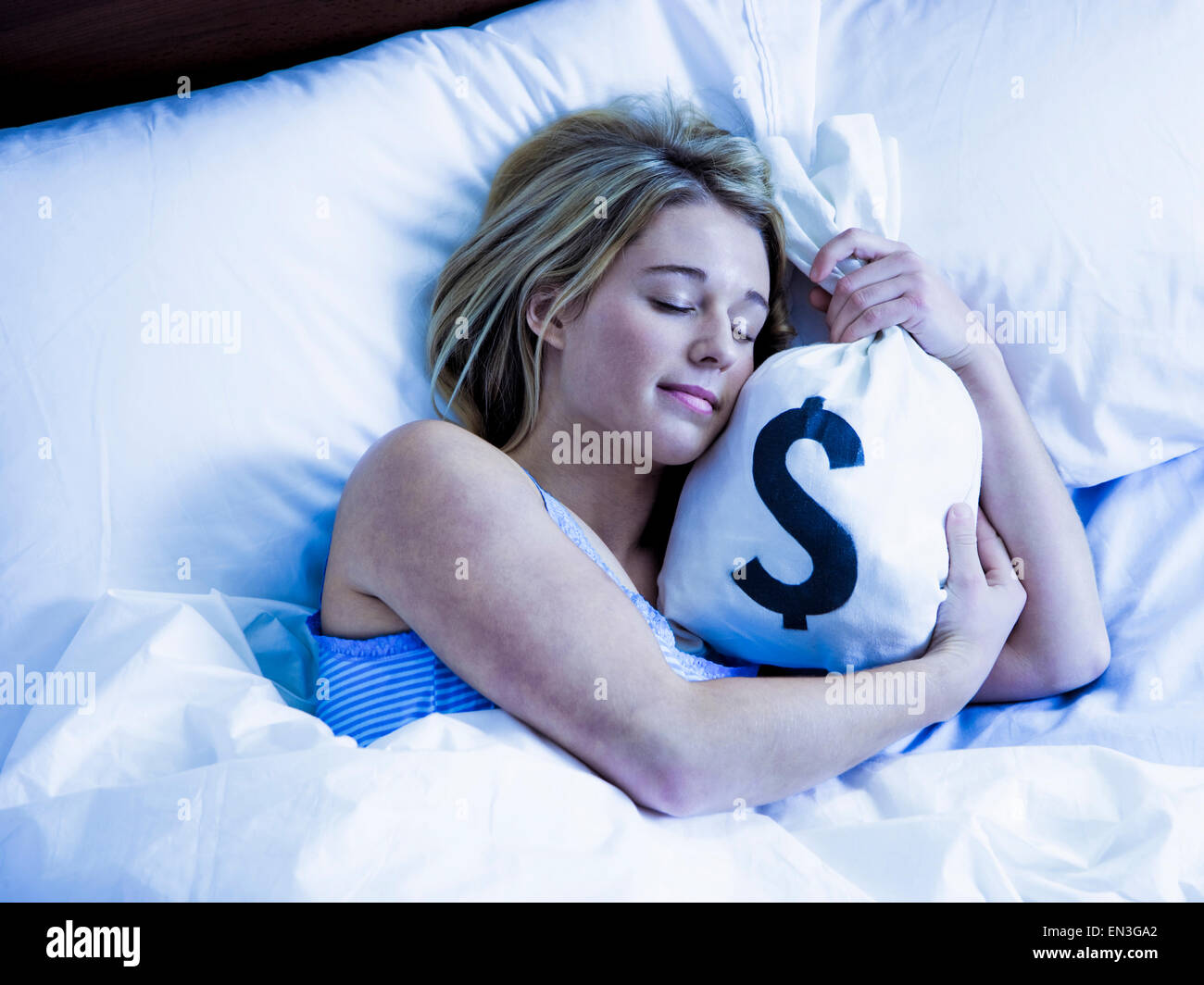 Young woman sleeping in bed with money bags Stock Photo