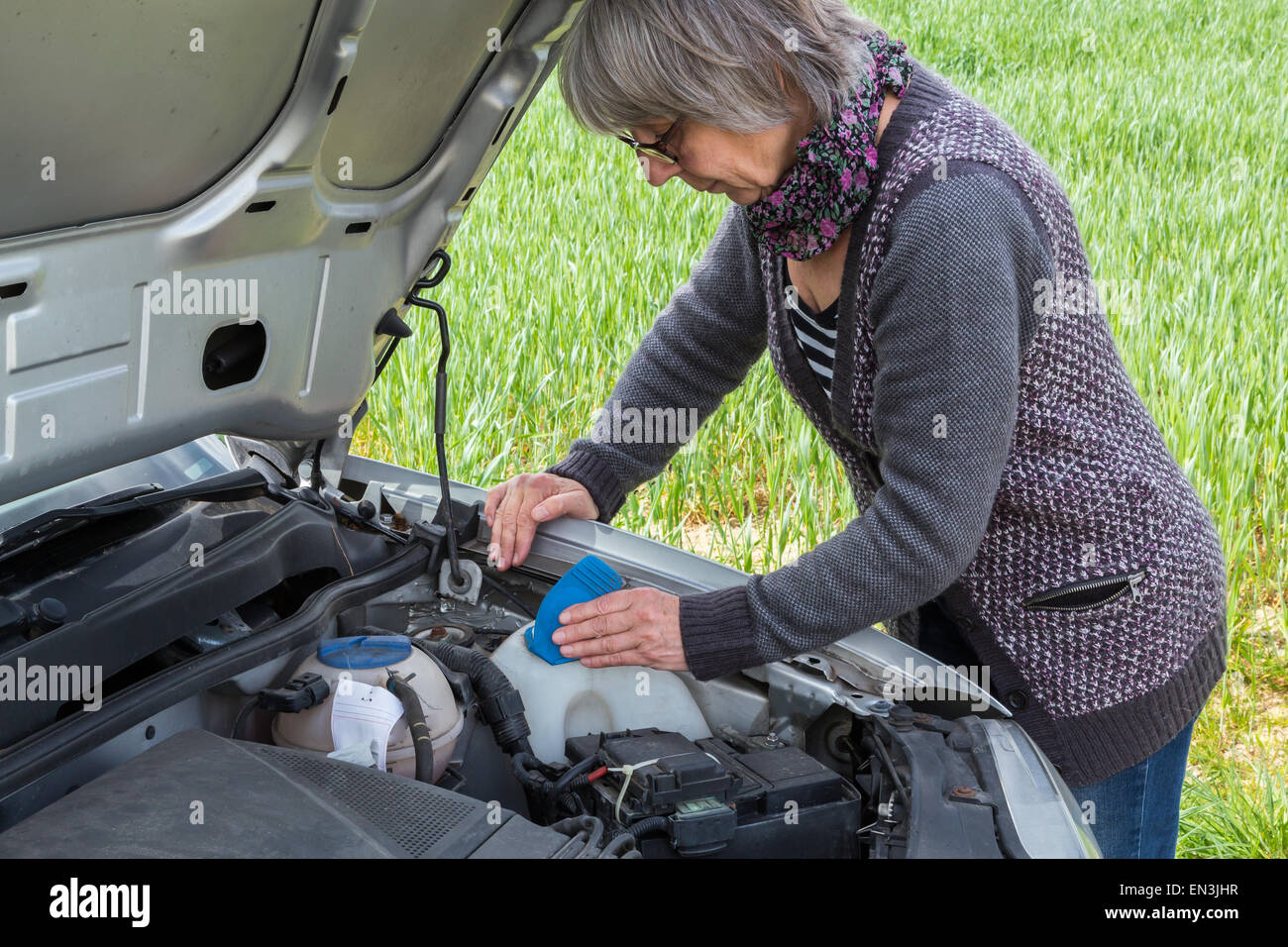 Senior Woman looks after the water level on the car. Stock Photo