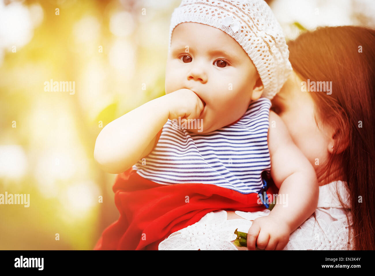 Beautiful cute baby girl in summer cap in the arms of her mother. Summer. Grain added for best impression. Stock Photo