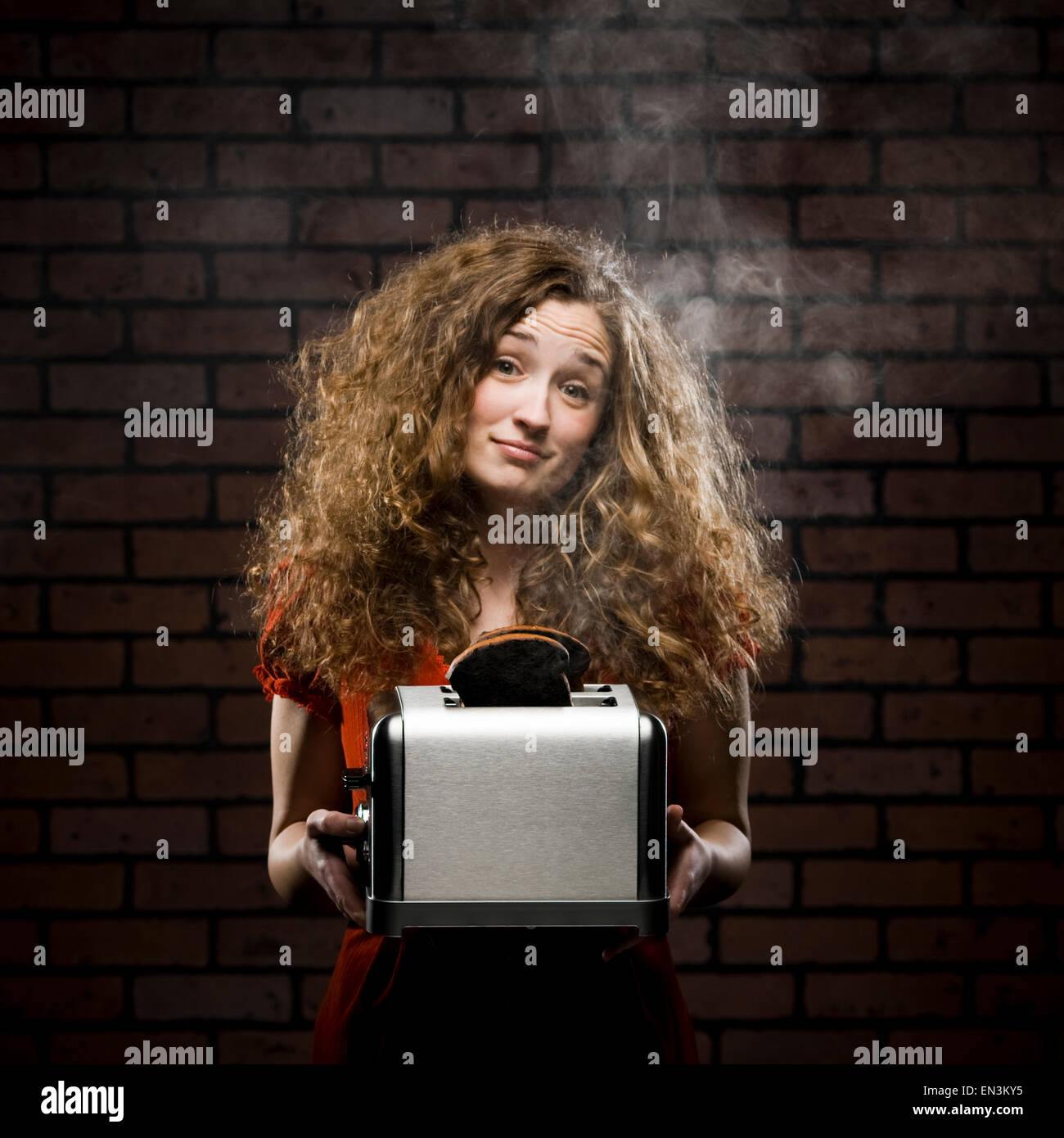 woman holding a smoking toaster with her hair all messed up Stock Photo