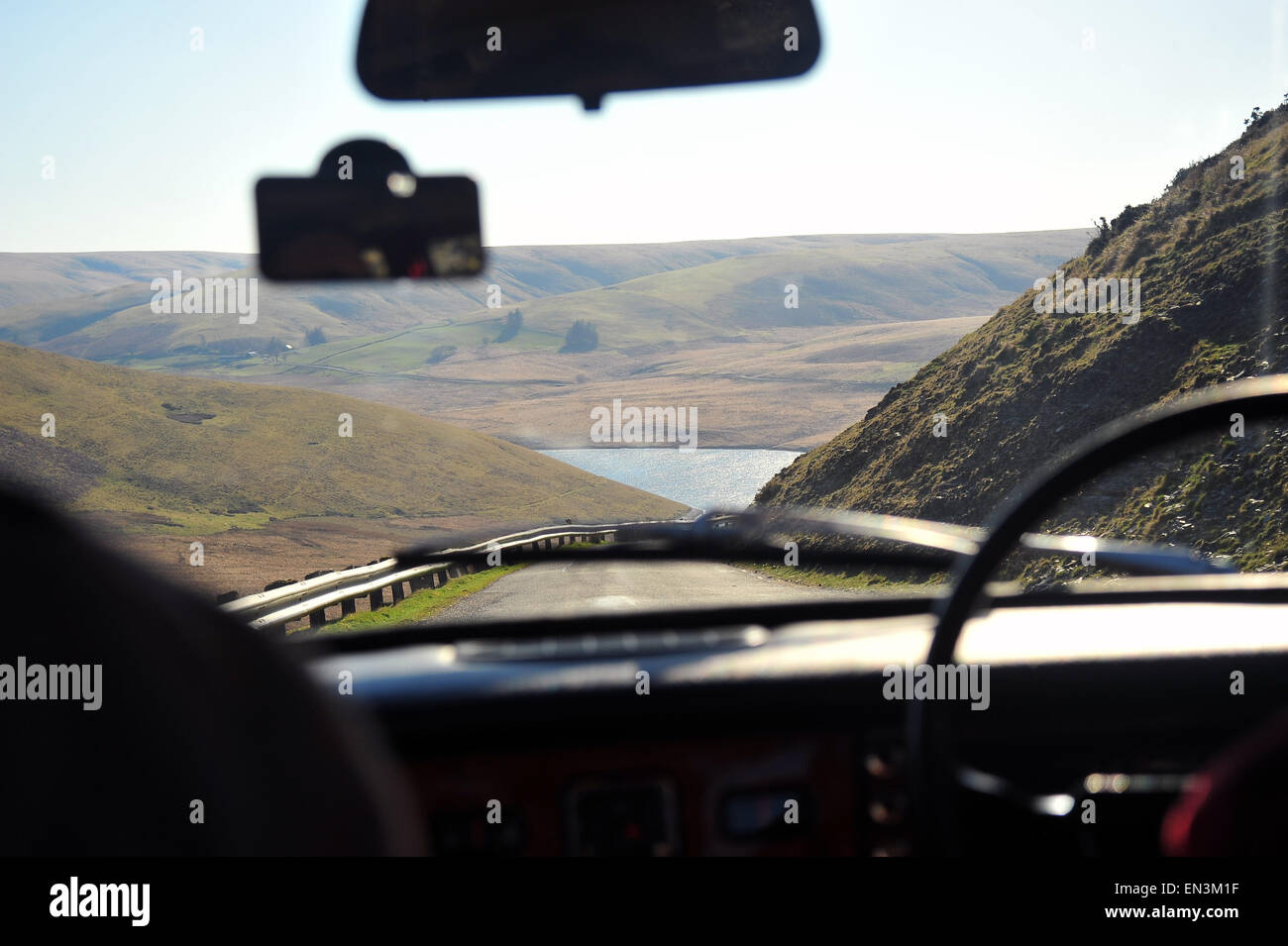 Hills and a lake visible through the front window of a car driving ...