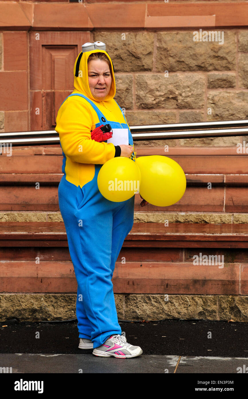 Woman wearing blue and yellow onesie holding yellow balloons at a charity even in Derry, Londonderry, Northern Ireland Stock Photo