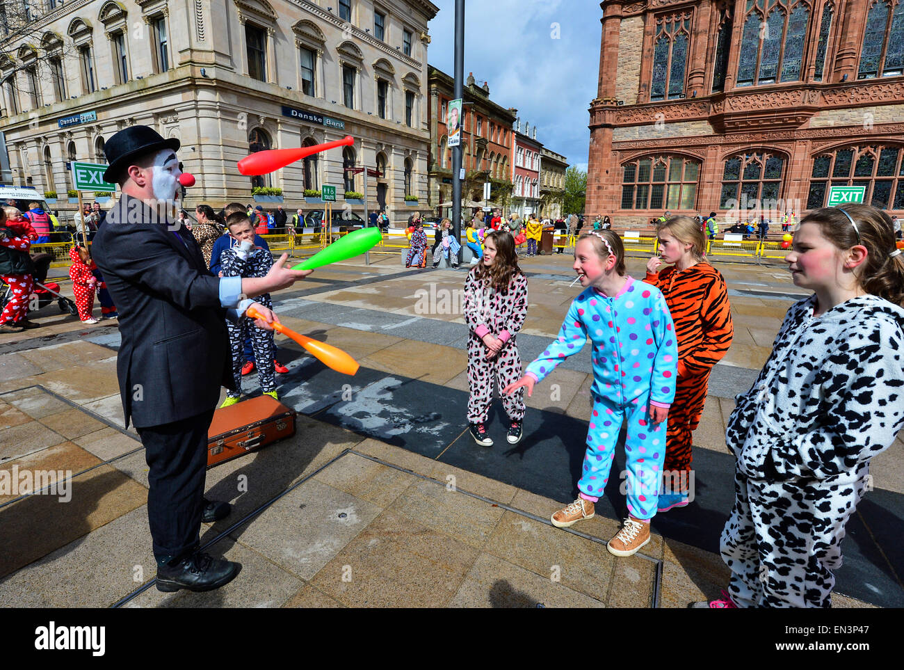 Clown with painted face, red nose and wearing a hat entertaining children dressed in onesies in the Guildhall Square, Derry, Lon Stock Photo