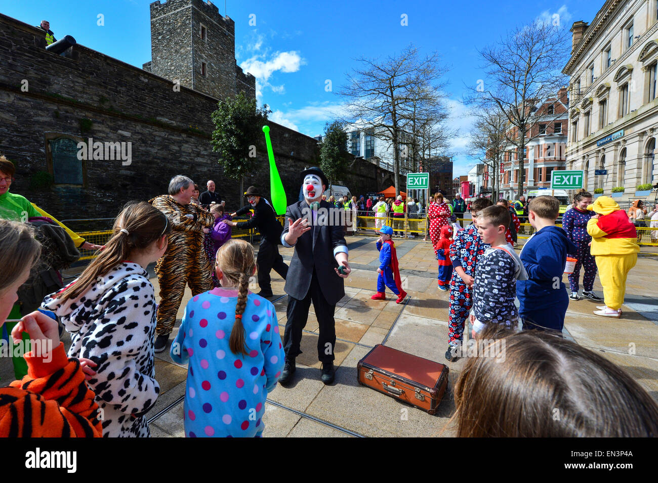 Clown with painted face, red nose and wearing a hat entertaining children dressed in onesies in the Guildhall Square, Derry, Lon Stock Photo