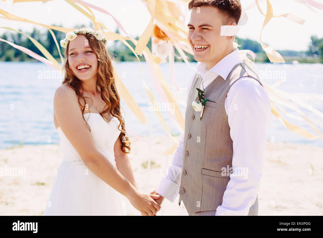 Happy wedding couple laughing and holding hands. Ceremony on open air. Selective focus on bride. Stock Photo