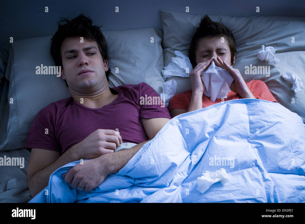 Man laying in bed with woman blowing nose with tissue Stock Photo