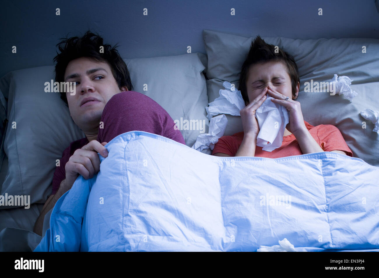 Man laying in bed with woman blowing nose with tissue Stock Photo