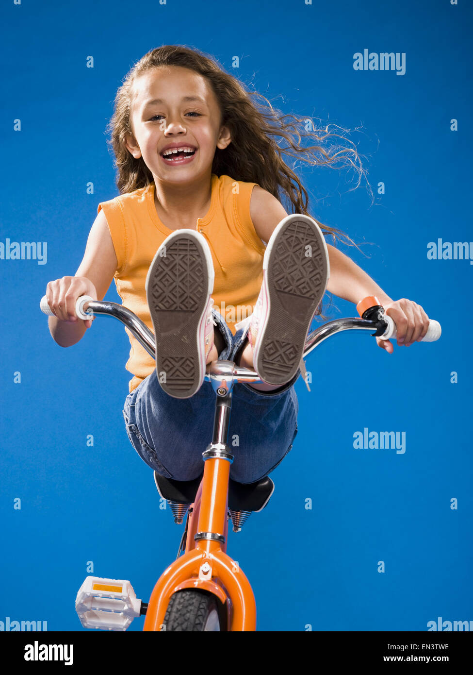 Girl riding orange bicycle with feet on handlebars smiling Stock Photo Alamy