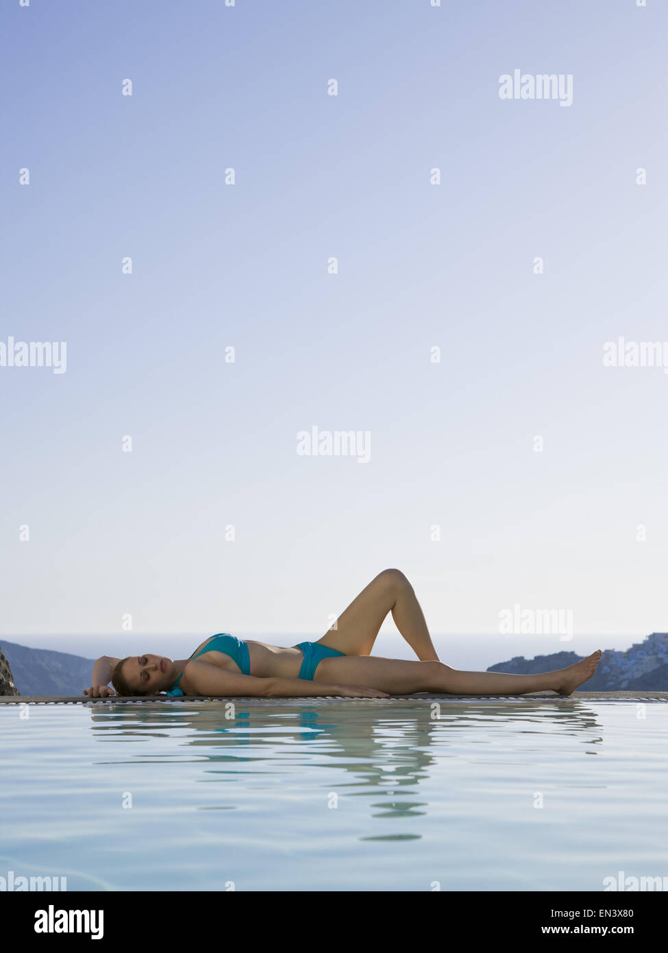 Woman in swimsuit lying down beside infinity pool outdoors Stock Photo