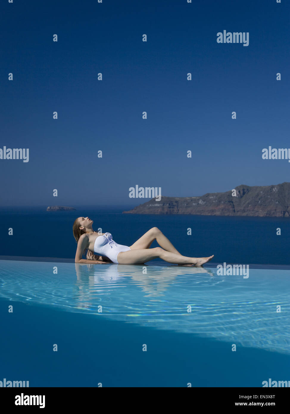 Woman in swimsuit reclining by infinity pool outdoors Stock Photo