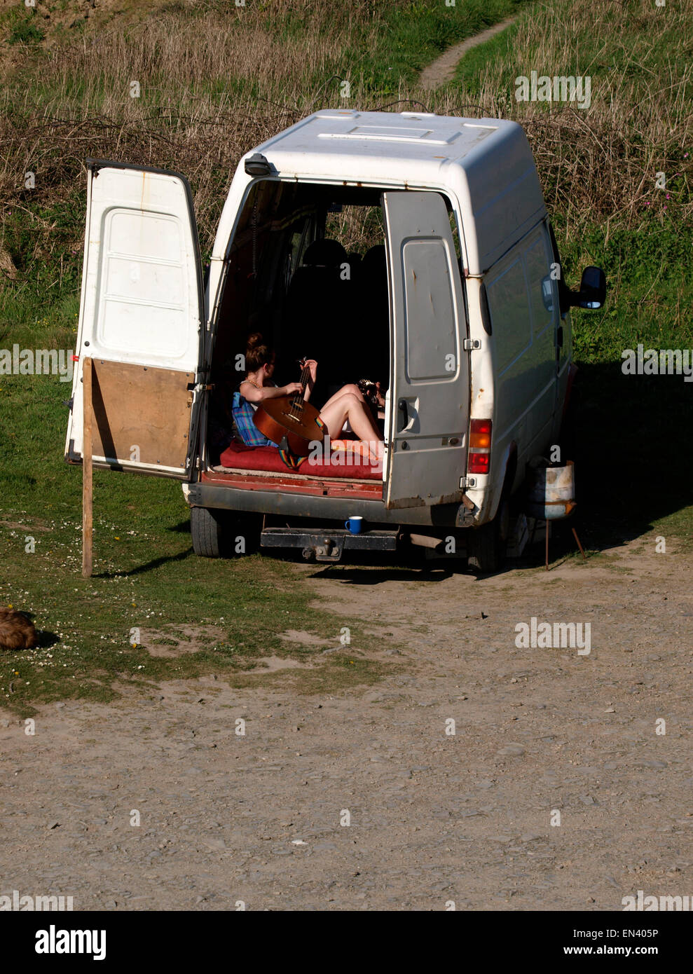 Young woman playing a guitar in the back of an old van, hippy style, Cornwall, UK Stock Photo