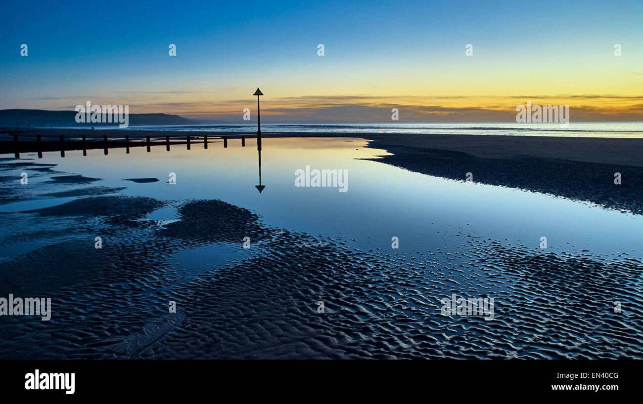 Reflections of groynes on the beach in Ynyslas, Wales at sunset shown ...