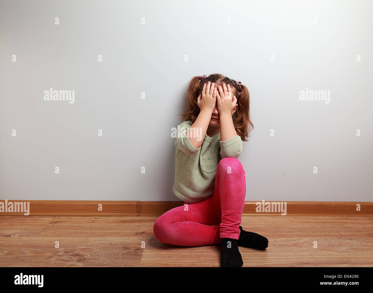 Crying unhappy kid girl sitting on the floor with closed face with empty copy space Stock Photo