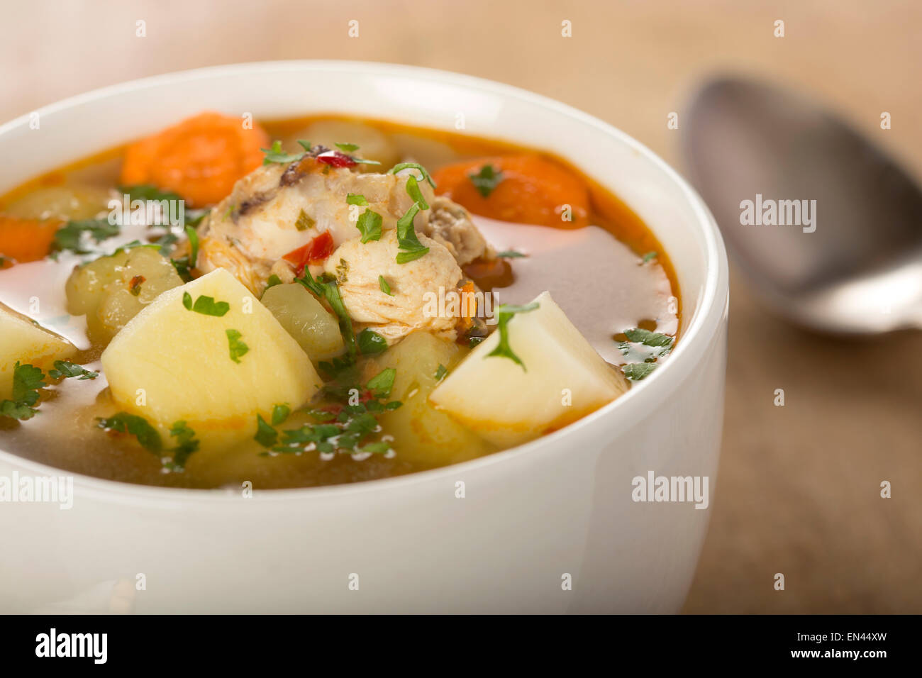 Homemade chicken soup in a white bowl with an antique soup spoon on a wooden table Stock Photo