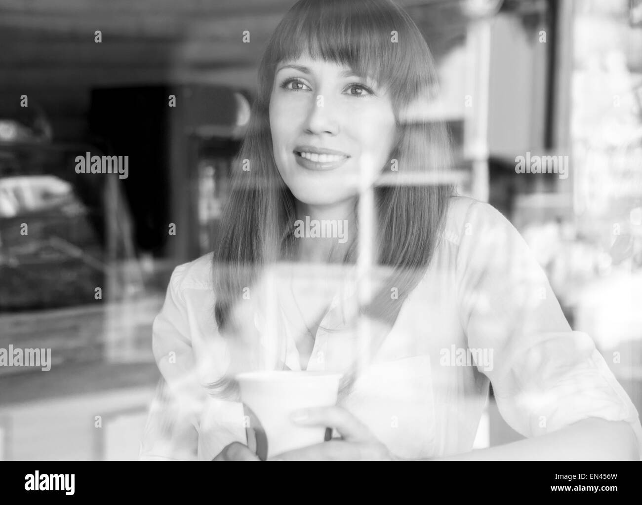 Young caucasian woman in coffee house at summer morning. Pretty girl with cup of coffee behind glass. Black and white image Stock Photo
