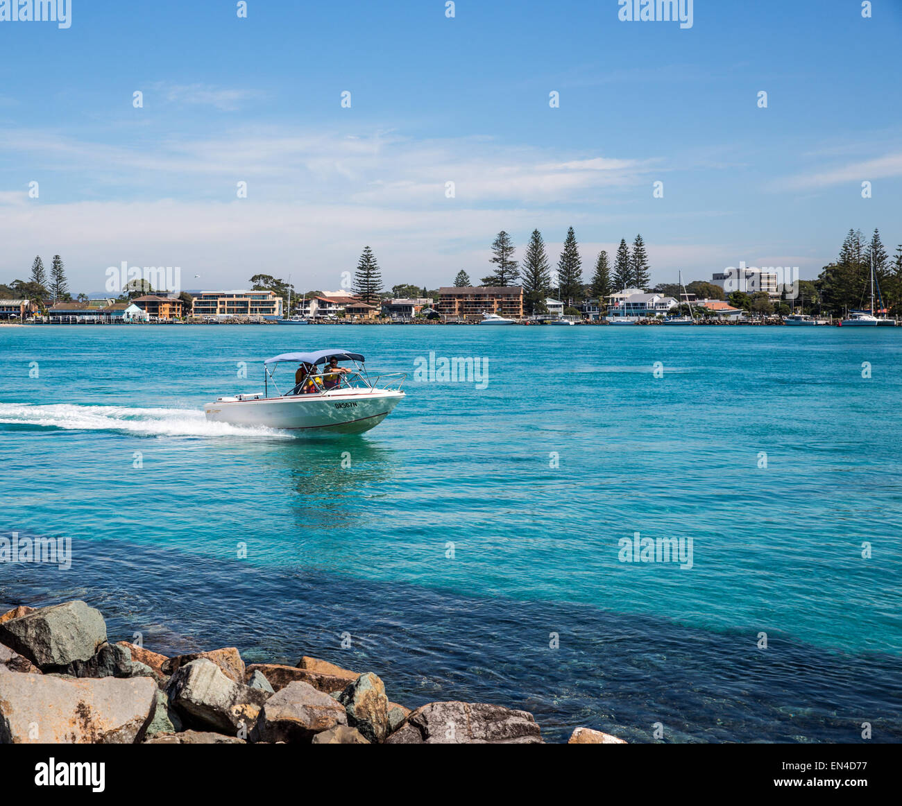A small boat travels Wallis Lake entrance and breakwater, Forster, NSW Australia Stock Photo