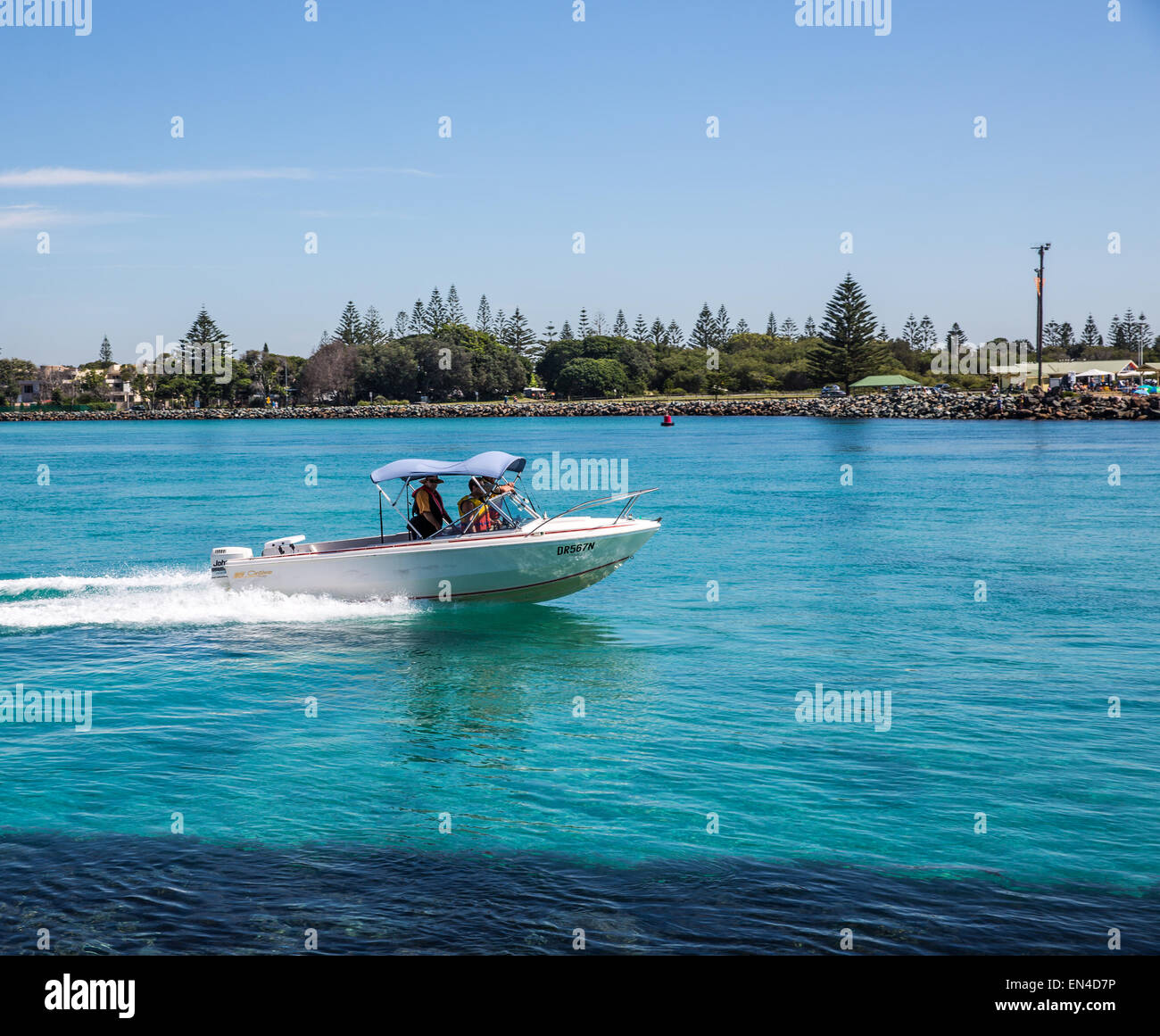 A small boat travels down Wallis Lake entrance and breakwater, Forster, NSW Australia Stock Photo
