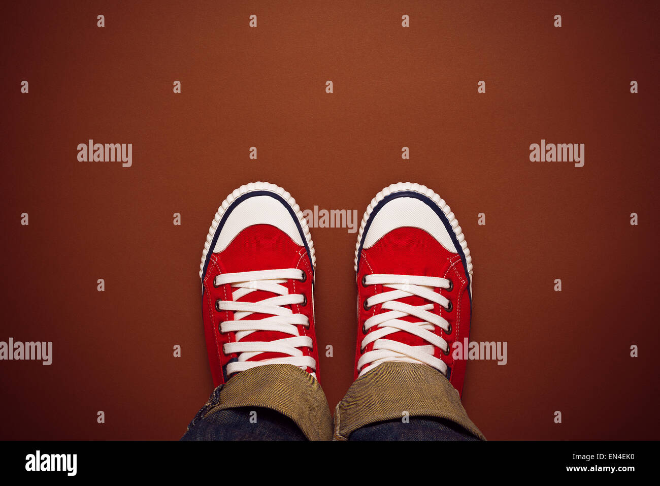 Feet From Above Concept, Teenage Person in Red Sneakers Standing on Brown Background, Blank Copy Space in Front, Top View Stock Photo