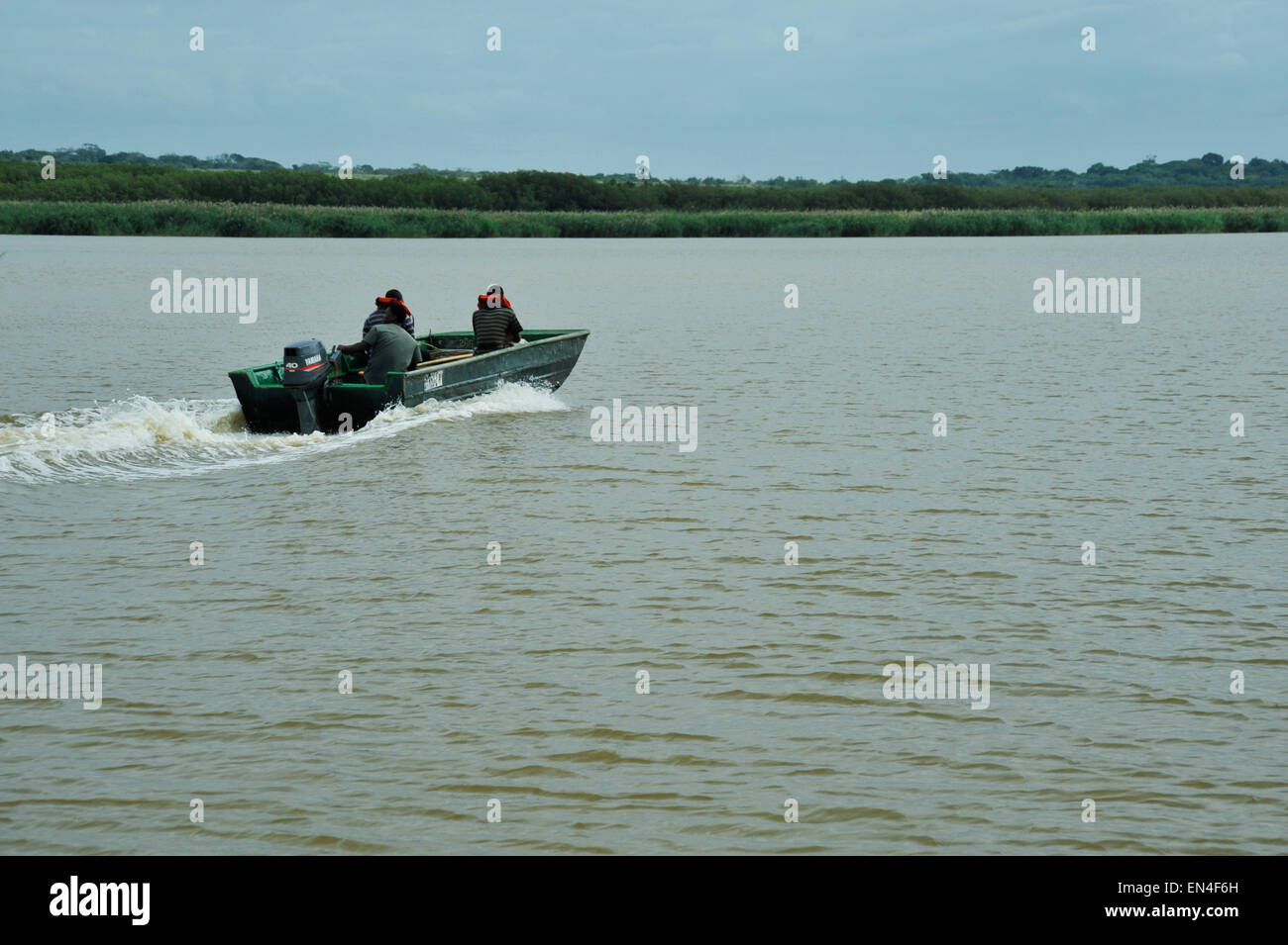 Three adult men in boat cruising on open brown water of iSimangoliso world heritage site, KwaZulu-Natal, South Africa Stock Photo