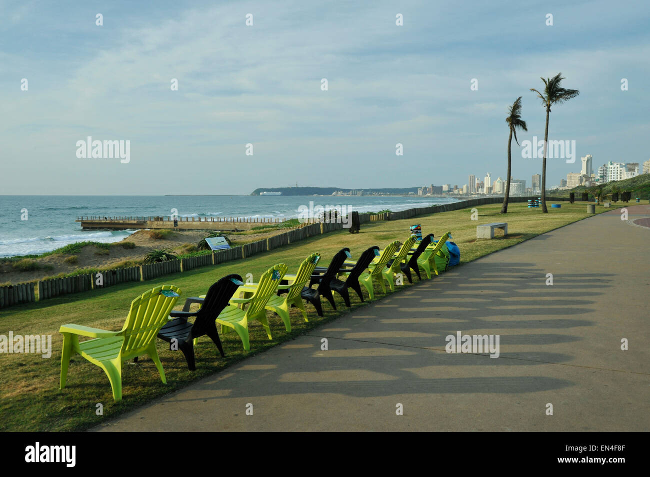 Row of green plastic chairs casting long shadows on seaside promenade