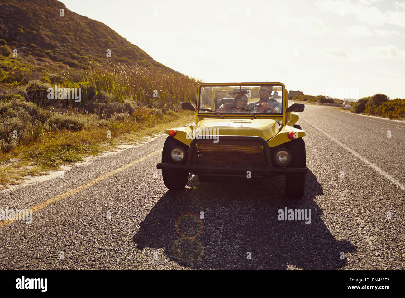 Young couple driving in a car on a open road. Young couple on road trip on summer day. Stock Photo