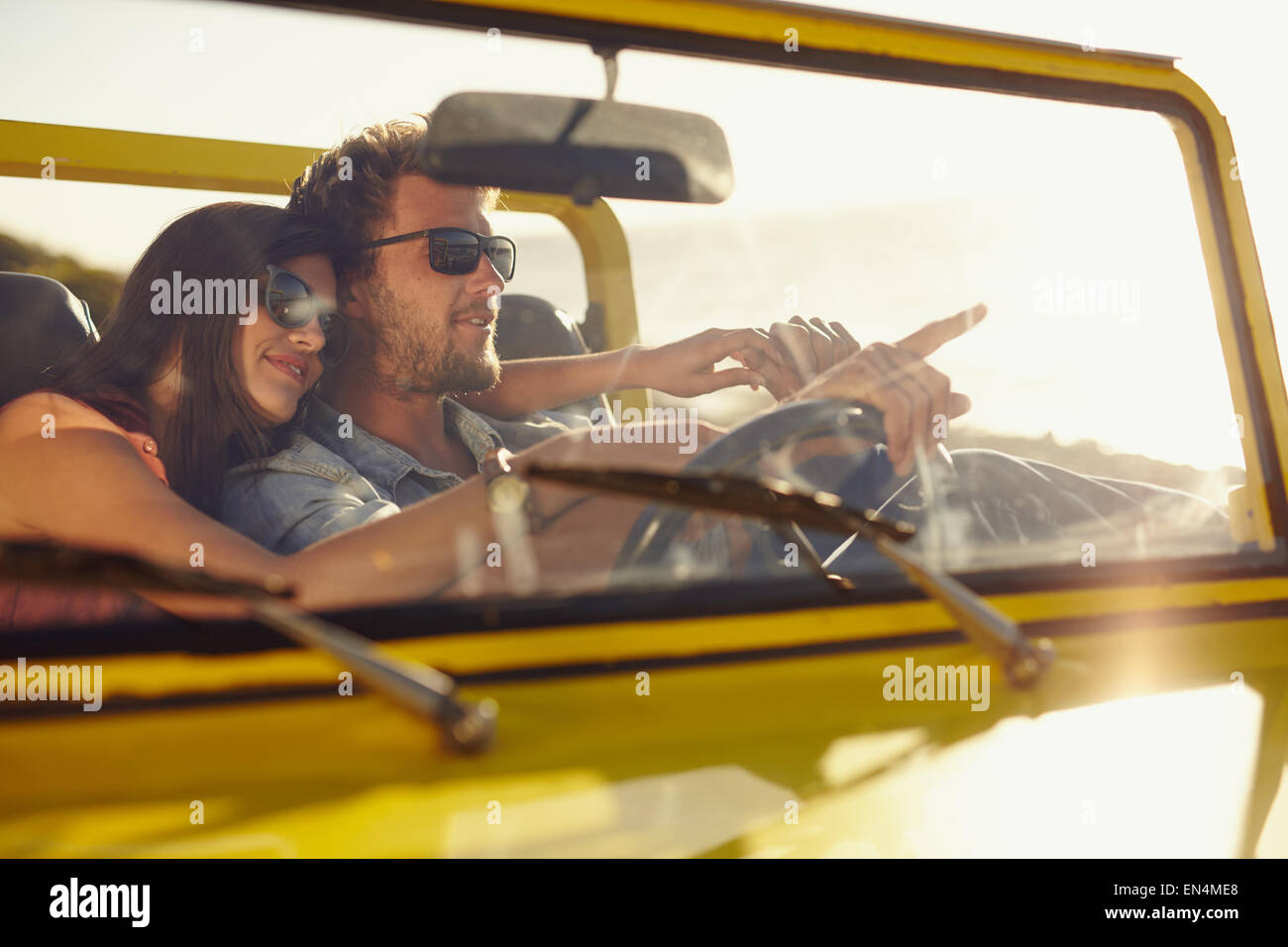 Young man driving car pointing something interesting to his girlfriend. Caucasian couple on summer holiday, Romantic couple. Stock Photo