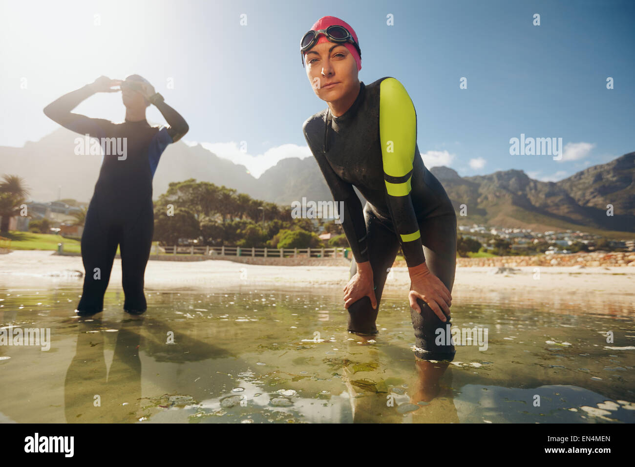 Confident young woman in wet suit standing in water looking at camera. Young triathletes preparing for competition. Triathlon tr Stock Photo