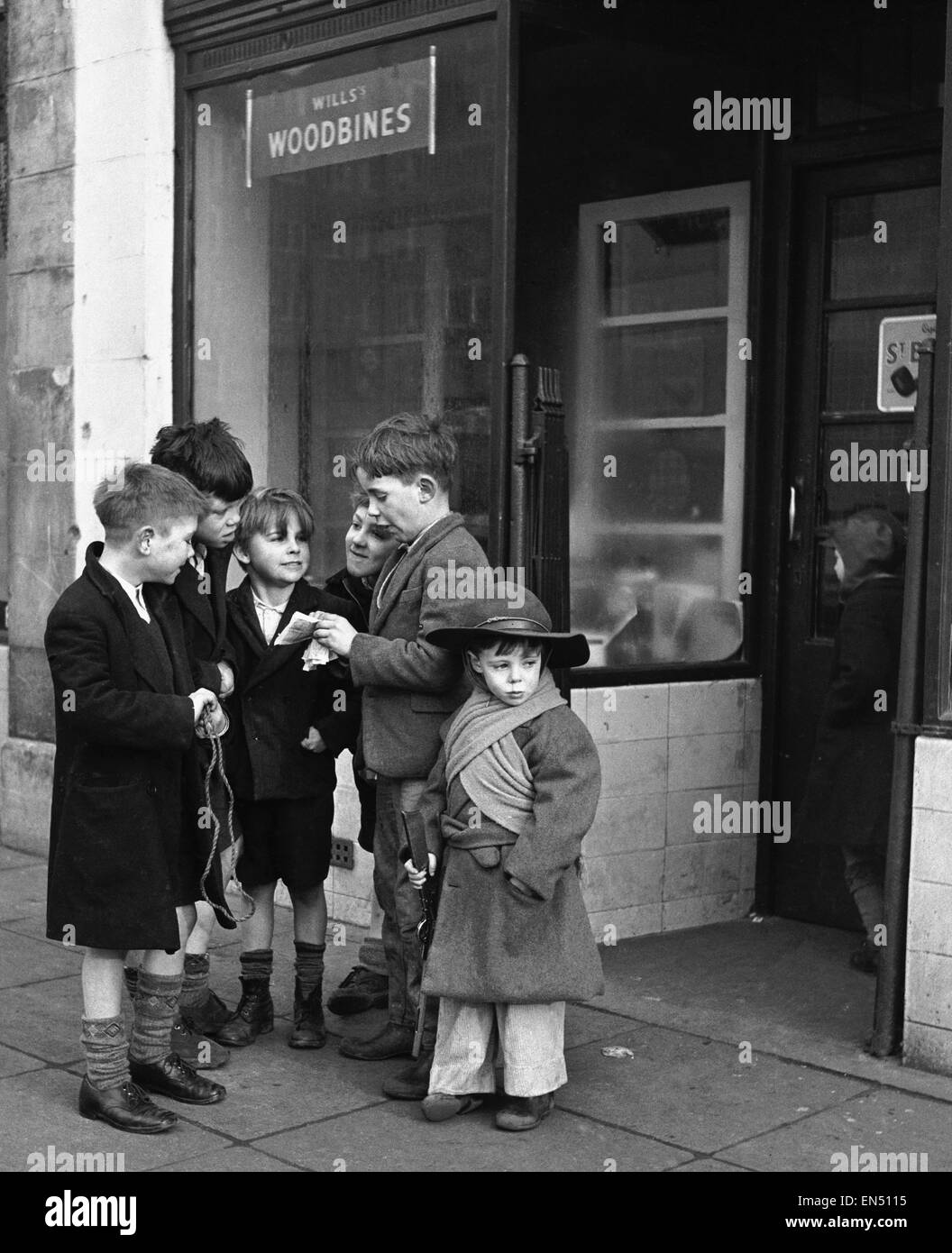 Life in the Mirror - Our Gang. 19th January 1954   A gang of boys plot todays agenda of mischief and mayhem outside a tobacconist in Bow Road in the East End of London.  Daily Mirror caption: 'This is The Conference. Not the stiff necked, prim and tight l Stock Photo