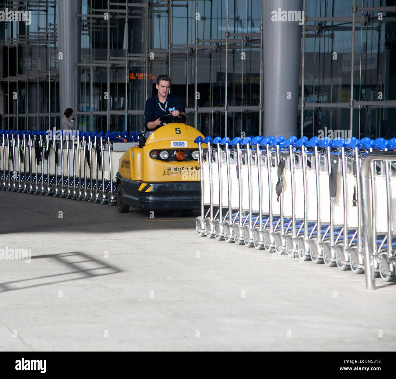 Man driving vehicle collecting trolleys at Malaga airport, Spain Stock Photo