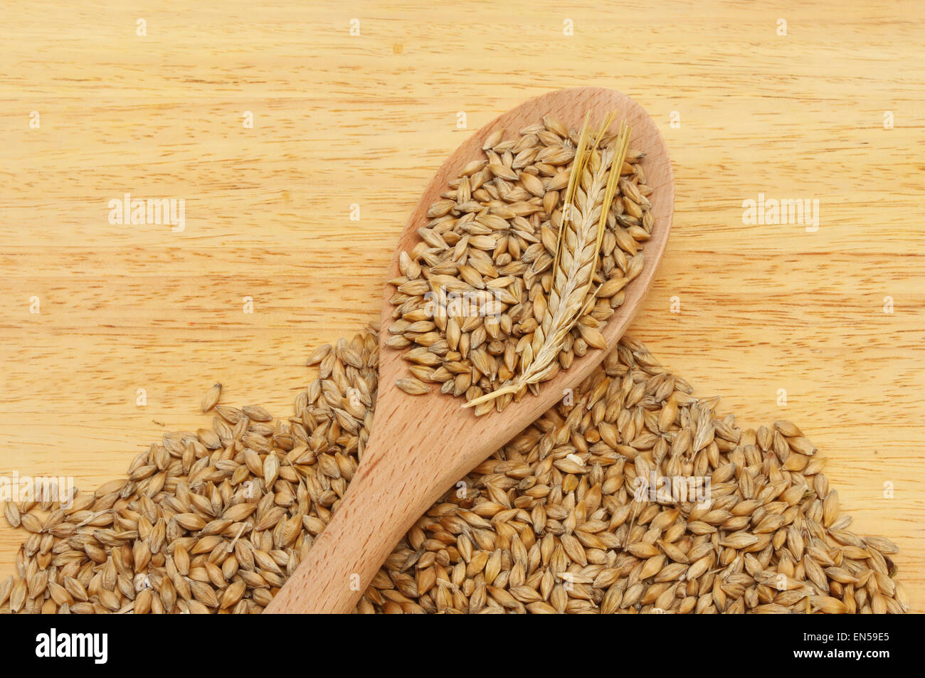 Grains and an ear of barley in and around a wooden spoon on a wooden board Stock Photo