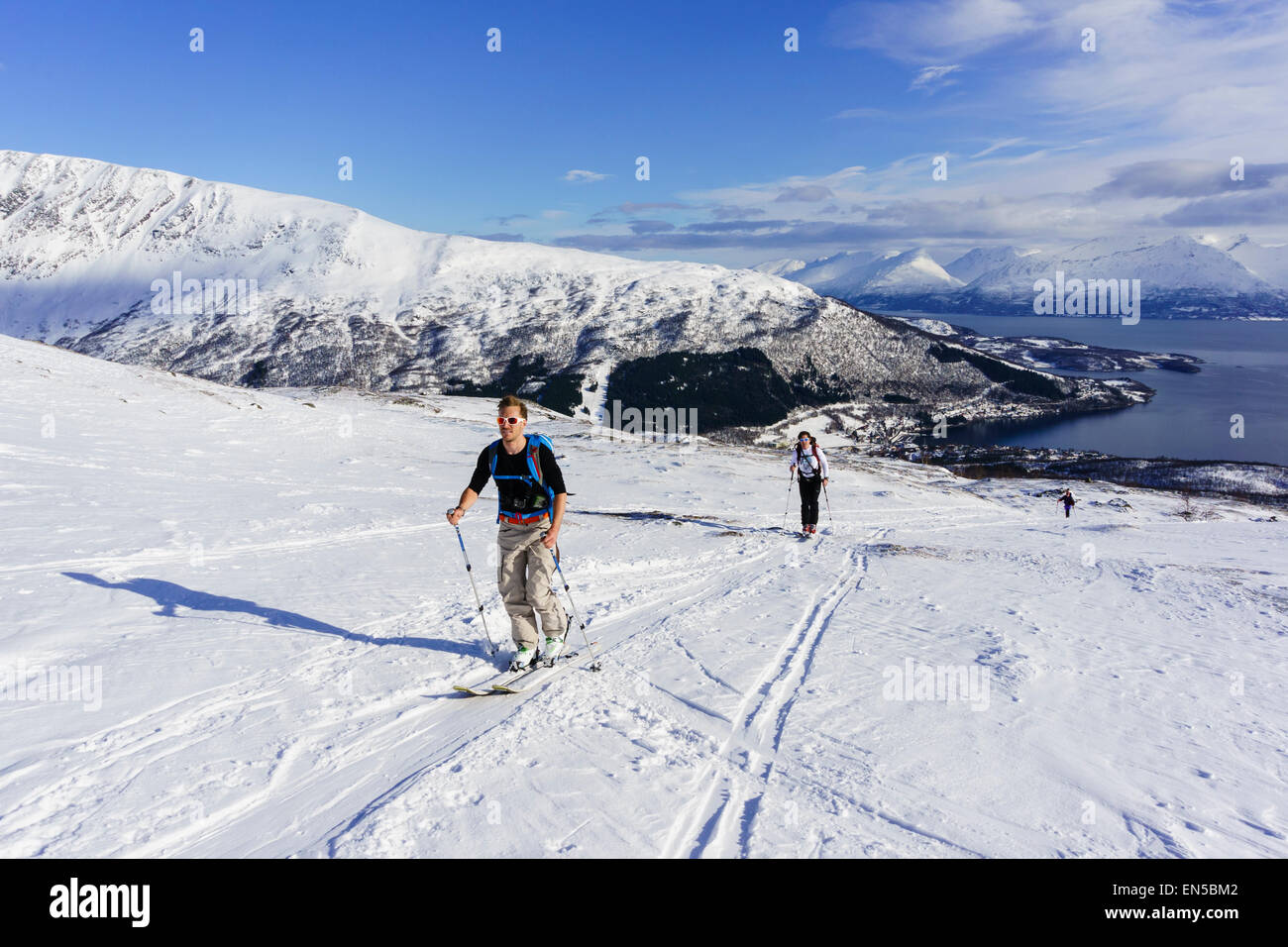 Skiers ski touring uphill with skins on the way up Rornefjellet mountain above Lyngenfjord. Lyngen Alps Troms County Norway. Stock Photo